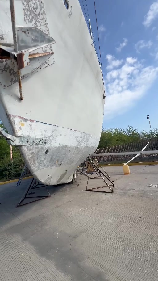 Near end-on view of Tortuga out of the water, showing the hull narrowing toward its lower edge and stands below.